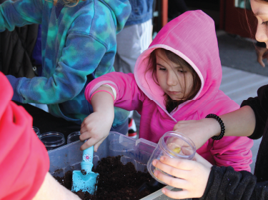 young girl in coat digging in soil